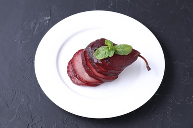 Tasty red wine poached pear and mint on black table, above view