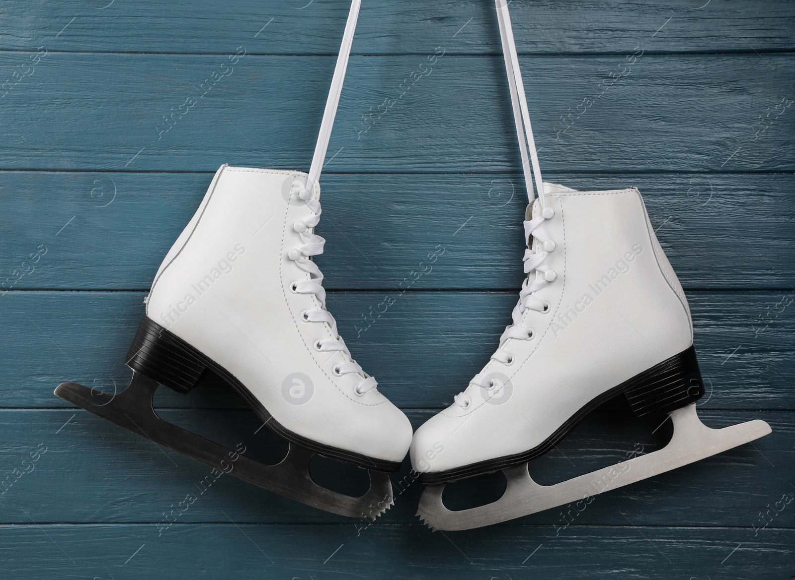 Photo of Pair of white ice skates hanging on blue wooden background