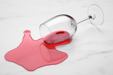 Glass with spilled red wine on white marble surface