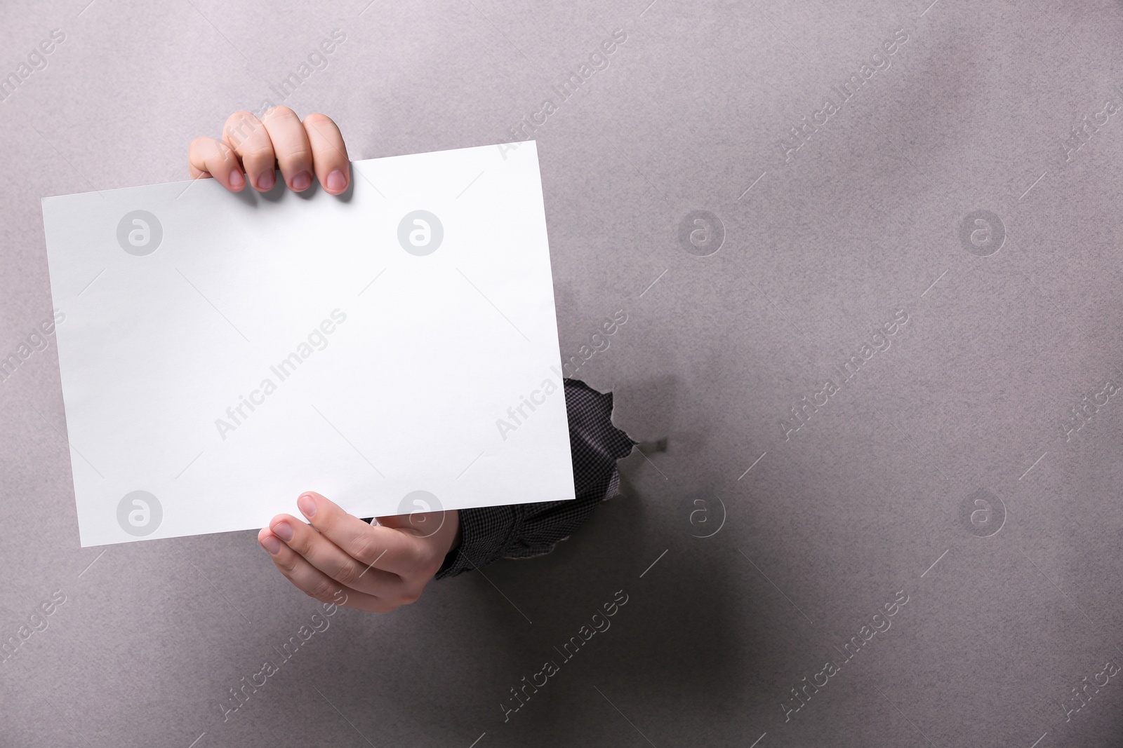Photo of Man holding sheet of paper through hole in white paper, closeup. Mockup for design