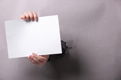 Man holding sheet of paper through hole in white paper, closeup. Mockup for design