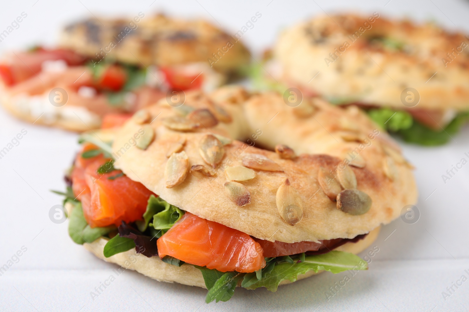 Photo of Tasty bagel with salmon and salad mix on white tiled table, closeup