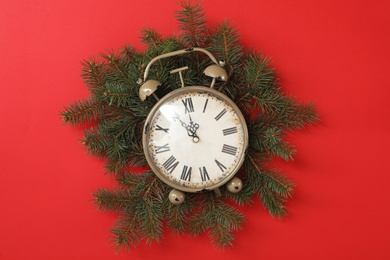 Photo of Alarm clock and fir tree branches on red background, flat lay. New Year countdown