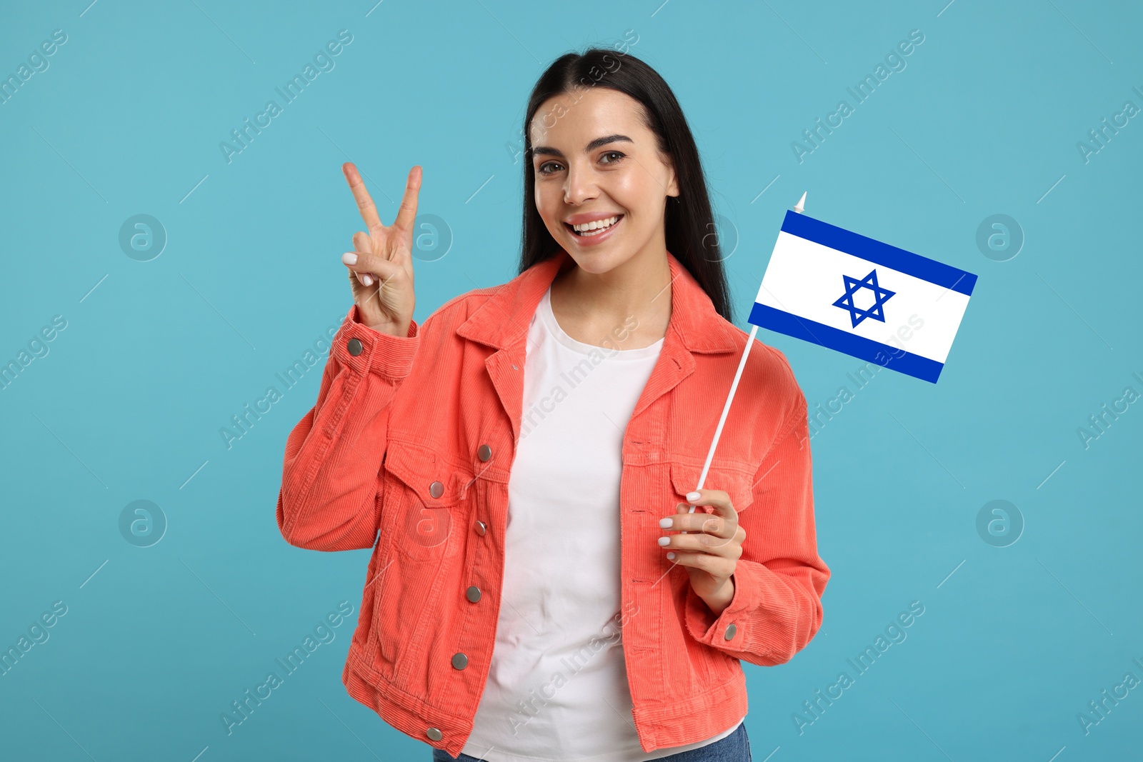 Image of Happy young woman with flag of Israel showing V-sign on light blue background