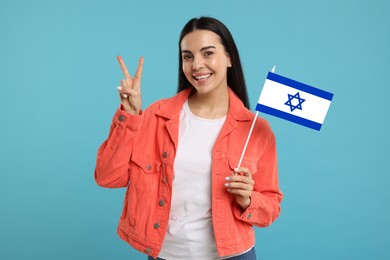 Happy young woman with flag of Israel showing V-sign on light blue background