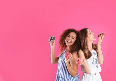 Beautiful young women with donuts on pink background