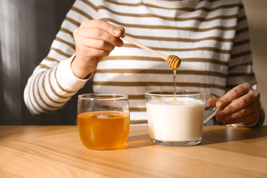 Photo of Woman adding honey to milk at wooden table closeup