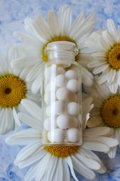 Photo of Bottle of homeopathic remedy and beautiful chamomiles on color background, closeup. Top view