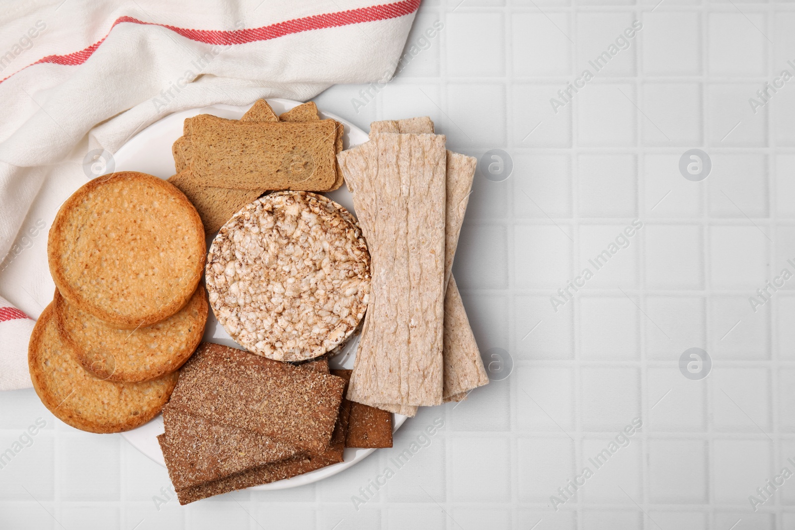 Photo of Rye crispbreads, rice cakes and rusks on white checkered table, flat lay. Space for text