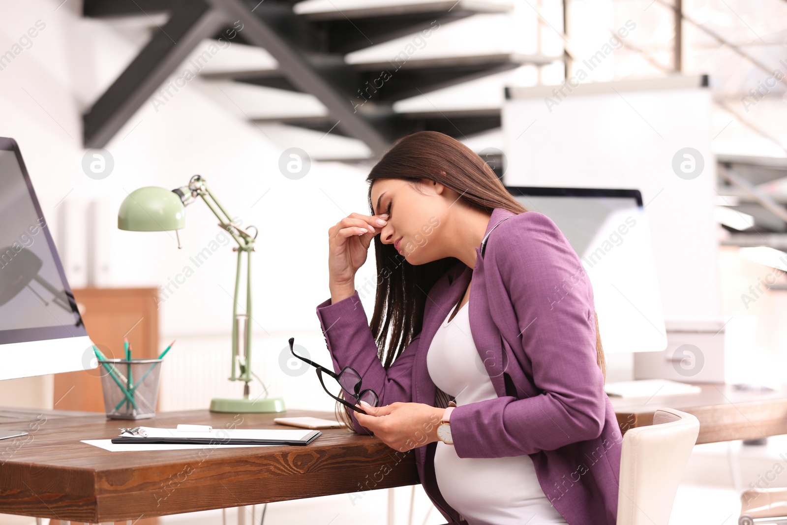 Photo of Young pregnant woman suffering from pain while working in office