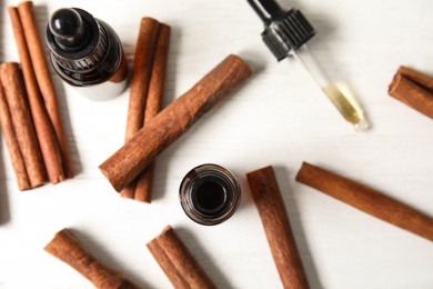 Photo of Bottles of essential oils and cinnamon sticks on white wooden table, flat lay