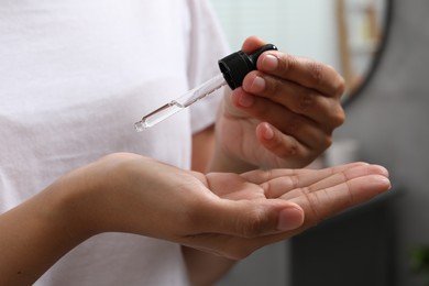 Photo of Woman applying cosmetic serum onto her hand on blurred background, closeup