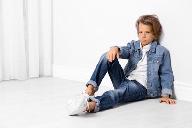 Photo of Cute little boy in casual outfit near white wall in room. Space for text