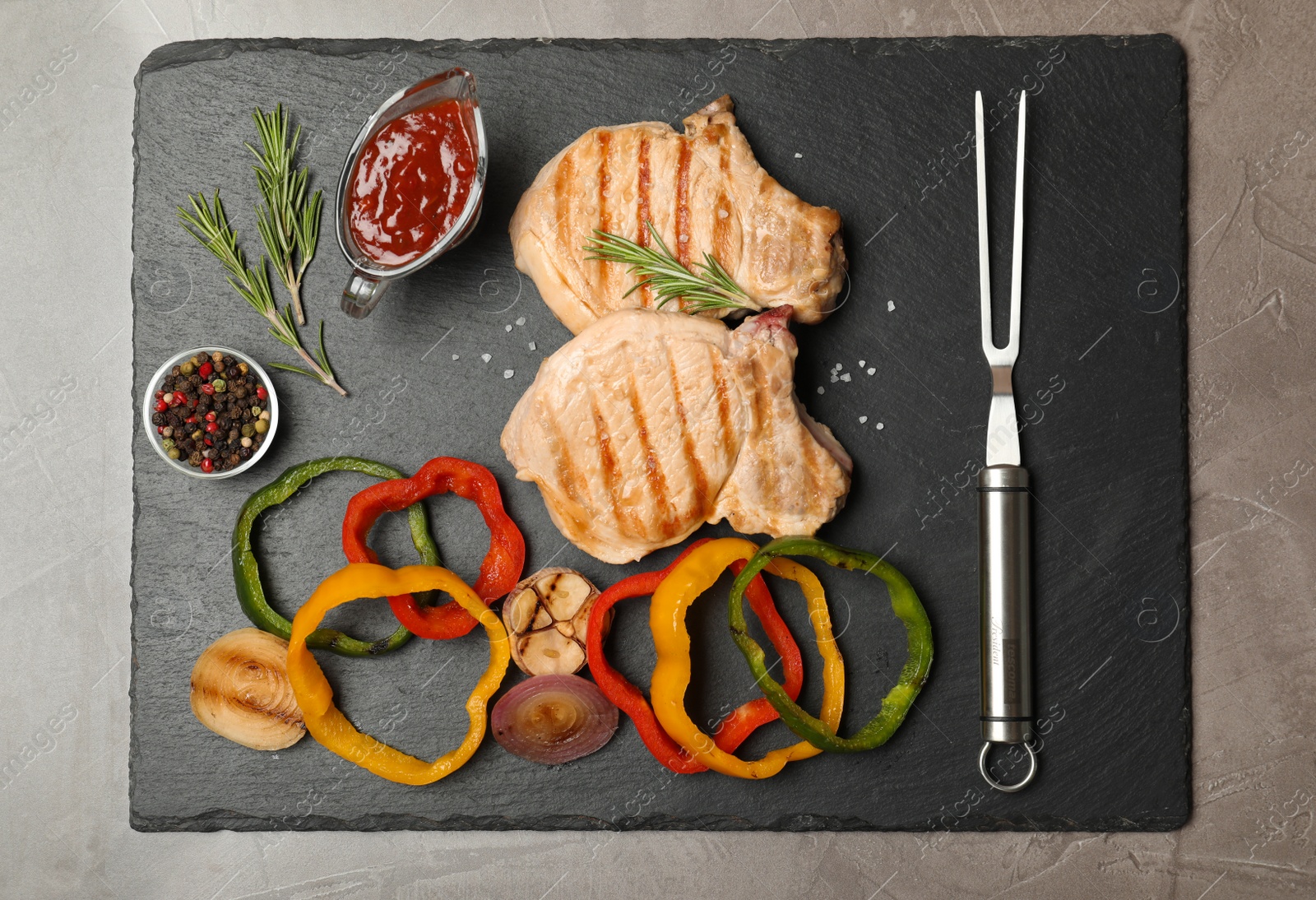 Photo of Slate plate with grilled meat, garnish and sauce on grey background, top view