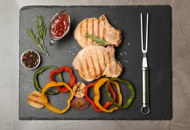 Slate plate with grilled meat, garnish and sauce on grey background, top view