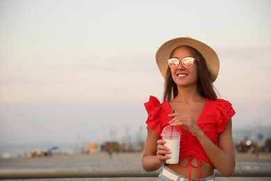 Photo of Beautiful young woman with tasty milk shake outdoors, space for text