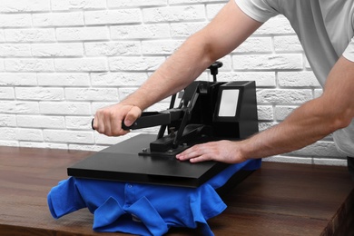 Photo of Man using heat press machine at table near white brick wall, closeup