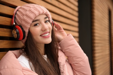 Photo of Young woman listening to music with headphones near wooden wall. Space for text