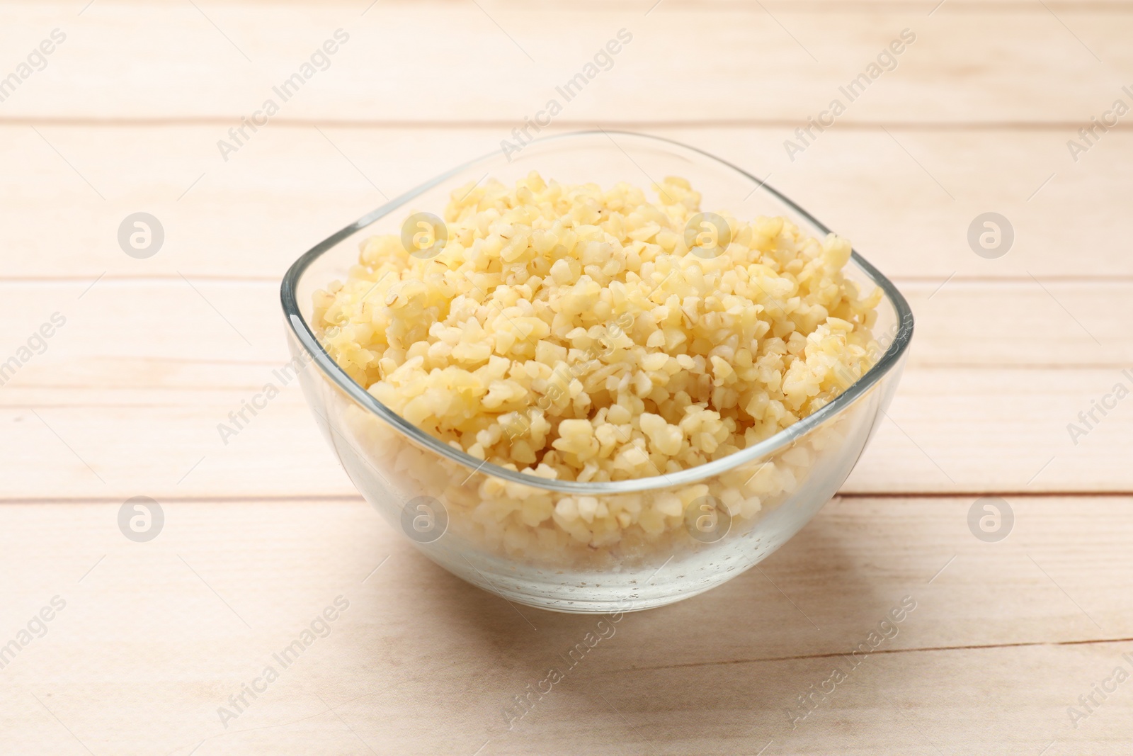 Photo of Delicious bulgur in glass bowl on wooden table, closeup