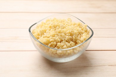 Delicious bulgur in glass bowl on wooden table, closeup