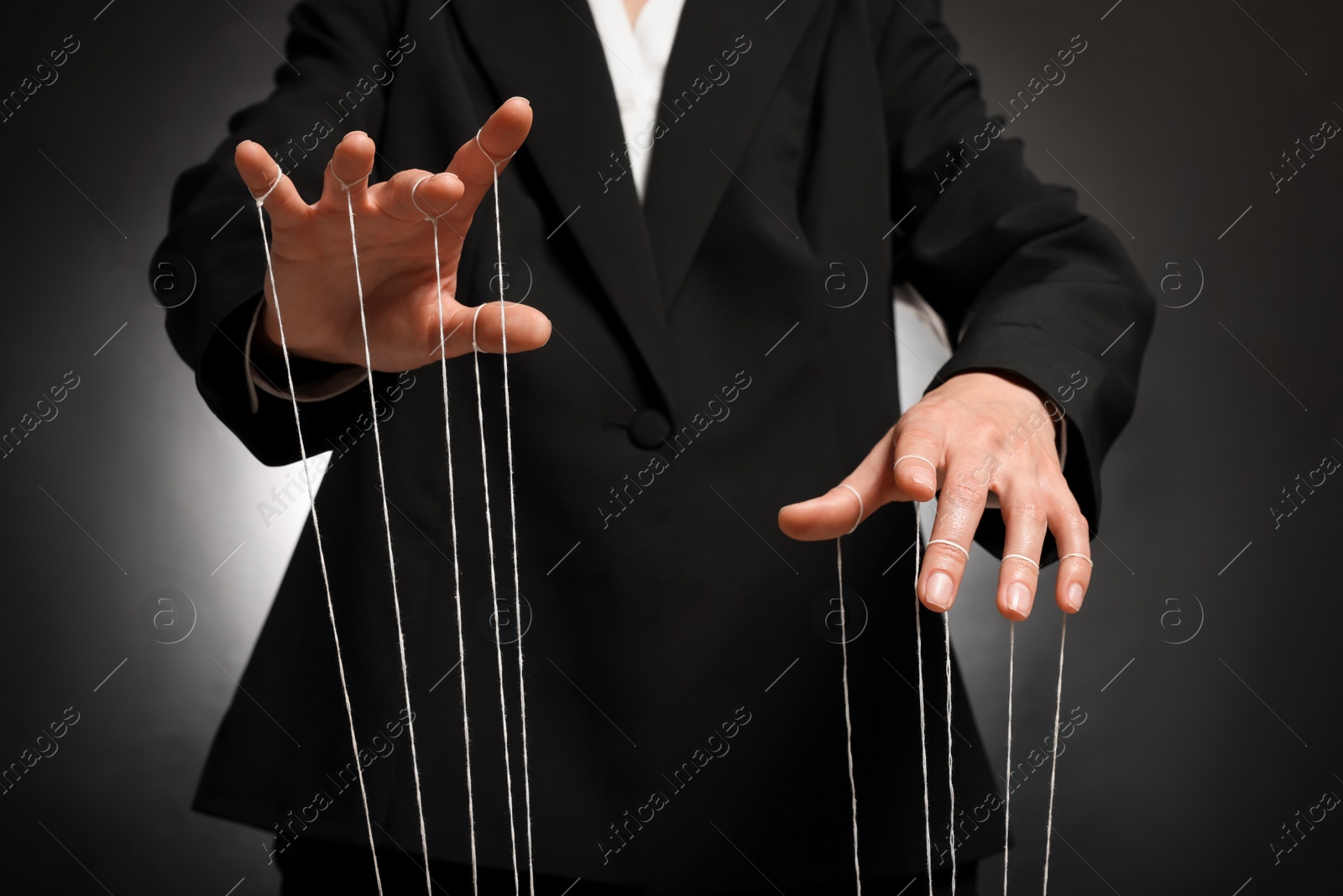 Photo of Woman in suit pulling strings of puppet on dark background, closeup