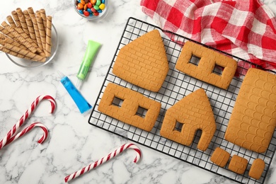 Parts of gingerbread house and ingredients for decoration on white marble table, flat lay