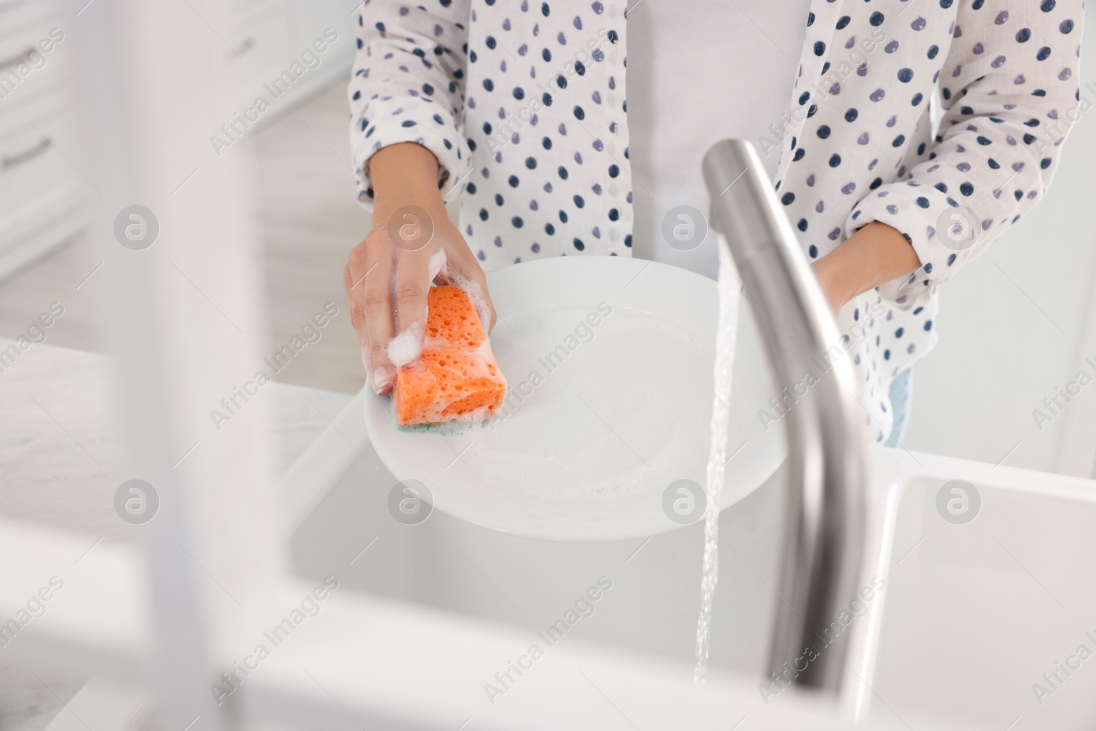 Photo of Woman washing plate above sink in modern kitchen, closeup