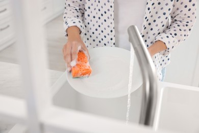 Woman washing plate above sink in modern kitchen, closeup