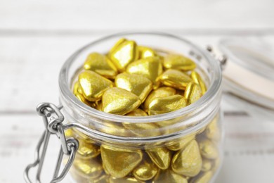 Photo of Jar with delicious heart shaped candies on white table, closeup