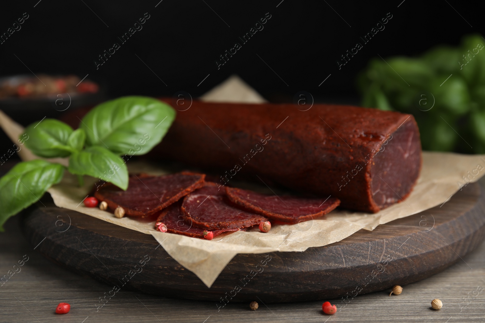 Photo of Delicious dry-cured beef basturma with basil and peppercorns on wooden table, closeup