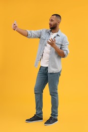 Young man taking selfie with smartphone on yellow background