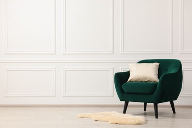Photo of Comfortable armchair with cushion near white wall indoors. Space for text