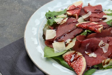 Photo of Plate with delicious bresaola salad on grey textured table, closeup