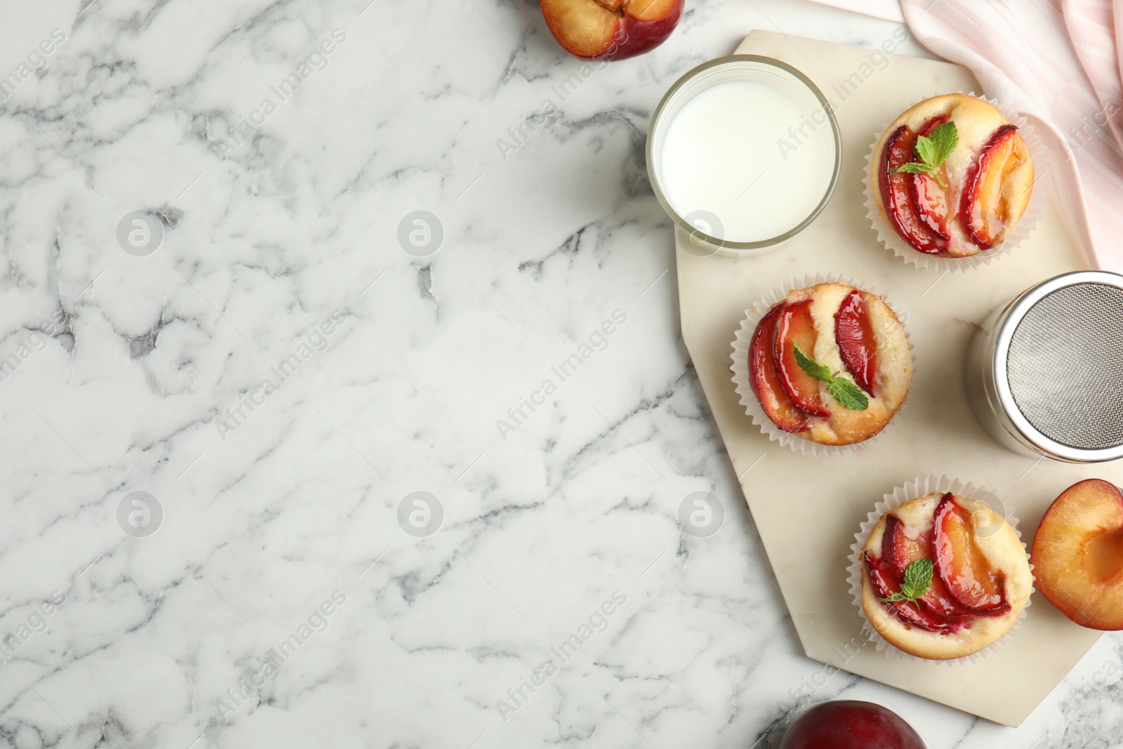 Photo of Delicious cupcakes with plums on white marble table, flat lay. Space for text