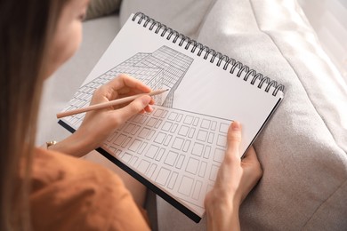 Woman sketching building in notebook with pencil at home, closeup