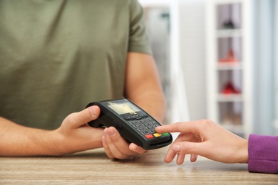 Photo of Woman using terminal for contactless payment in shop, closeup