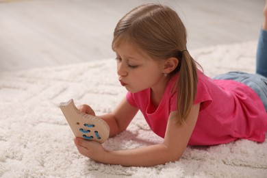 Photo of Cute little girl playing with wooden lacing toy on carpet indoors
