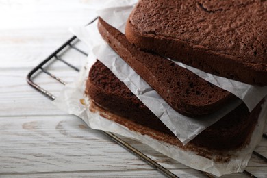 Photo of Layers of homemade chocolate sponge cake on white wooden table, closeup. Space for text