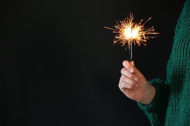 Photo of Woman holding burning sparklers on black background, closeup. Space for text