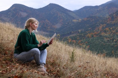 Young woman drawing on tablet in mountains, space for text