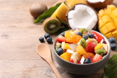 Photo of Bowl of delicious fruit salad on wooden table, space for text