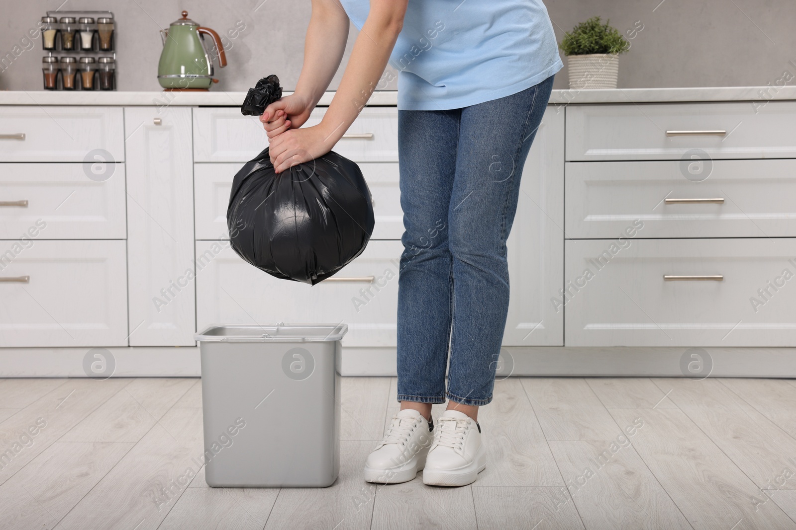 Photo of Woman taking garbage bag out of trash bin in kitchen, closeup