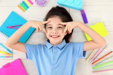 Cute little girl with school stationery on wooden background, top view