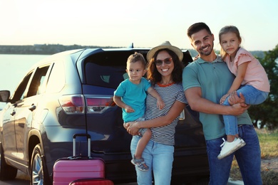 Photo of Happy family with suitcases near car on riverside