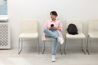 Photo of Woman with cup of drink waiting for appointment indoors