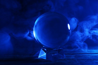 Photo of Magic crystal ball on wooden table and smoke against dark background. Making predictions