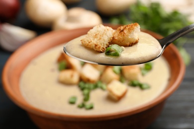 Photo of Spoon with fresh homemade mushroom soup over bowl, closeup
