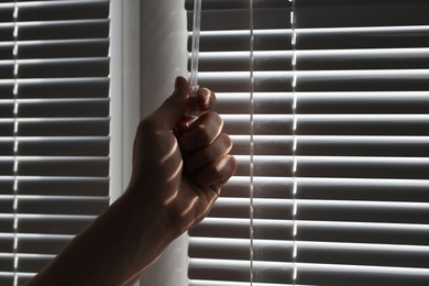 Man opening white blinds at home, closeup