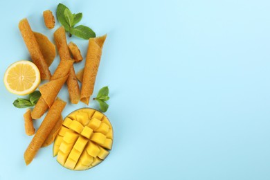 Photo of Delicious fruit leather rolls, mango, mint and lemon on light blue background, flat lay. Space for text