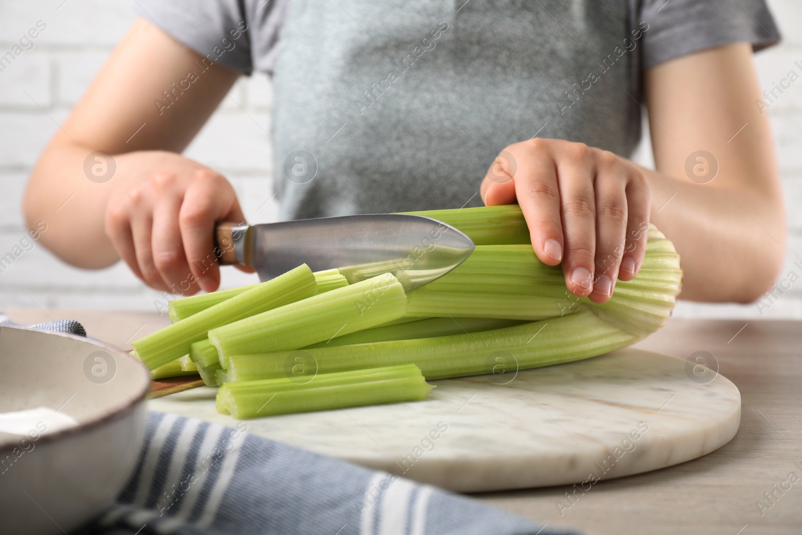 Photo of Woman cutting fresh green celery at white table indoors, closeup